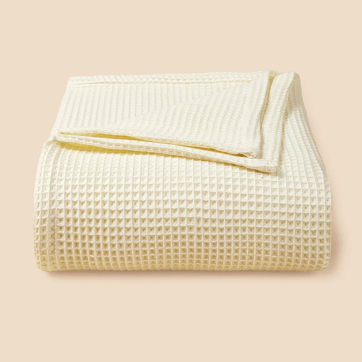 A white lightweight cotton waffle blanket folded neatly on a beige background.