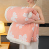 A woman is holding a thick pink and white jacquard lambswool blanket, featuring a floral pattern, against a light background.