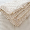 A stack of cream-colored floral print muslin blankets folded on a white surface.