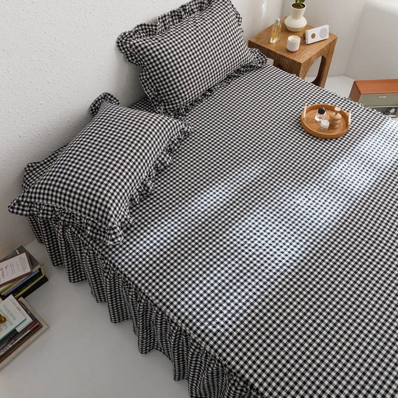 A black and white plaid cotton bed skirt cover with ruffled edges and decorative pillows.
