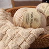 A ball of beige wool thread labeled Delicate and Soft, resting on a woven basket.