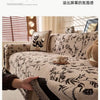 A close-up of a beige chenille sofa slipcover featuring a black floral pattern and dark trim, with a hand touching the fabric