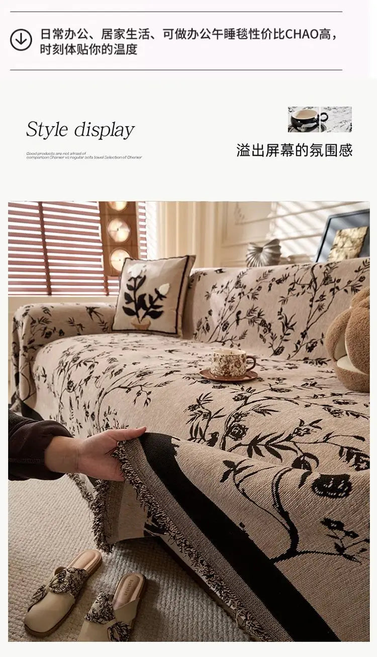 A close-up of a beige chenille sofa slipcover featuring a black floral pattern and dark trim, with a hand touching the fabric