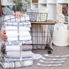 A stack of white and gray bed sheets organized with black straps in a wire basket.