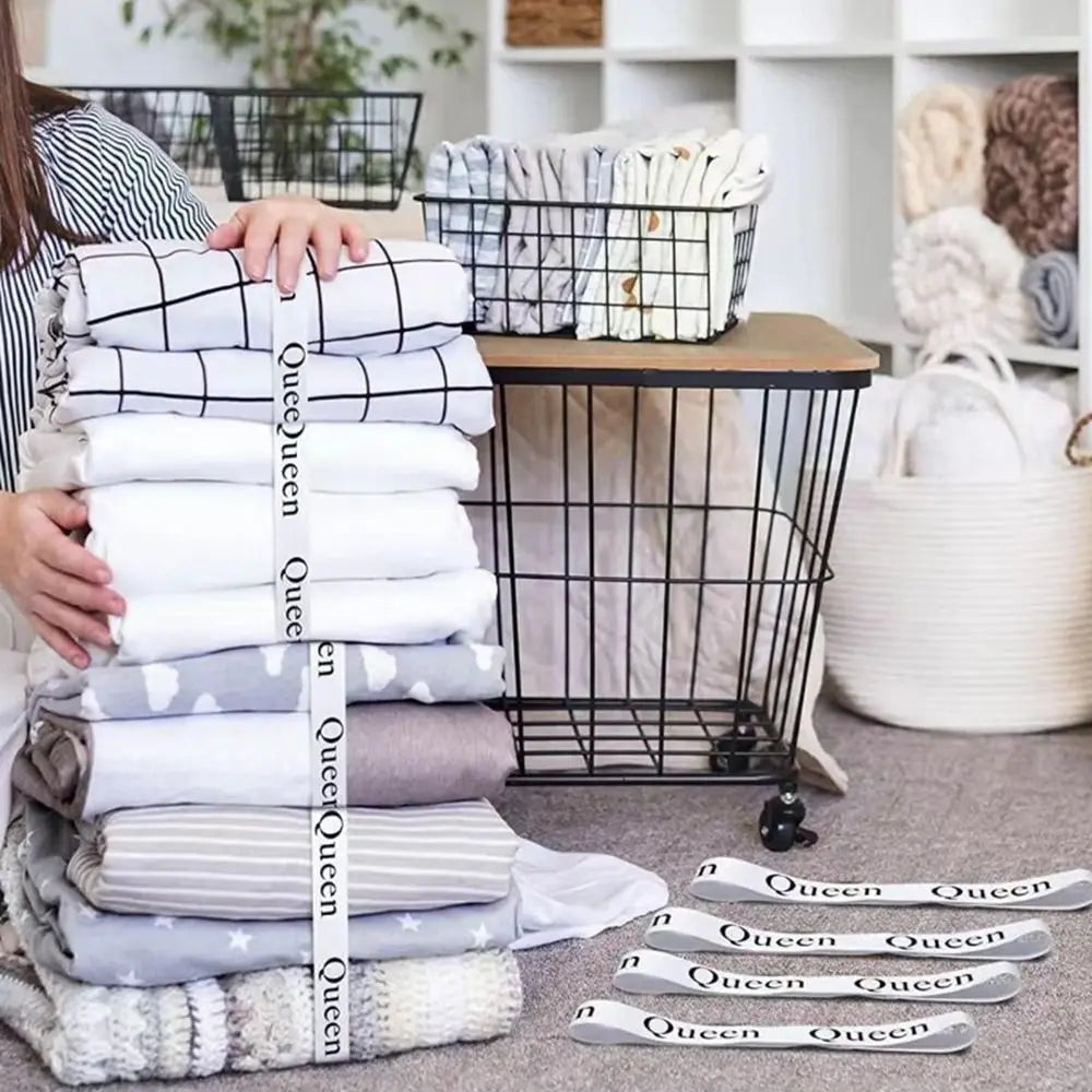 A stack of white and gray bed sheets organized with black straps in a wire basket.