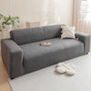A modern gray sofa with a light beige throw pillow and decorative items on a white rug.