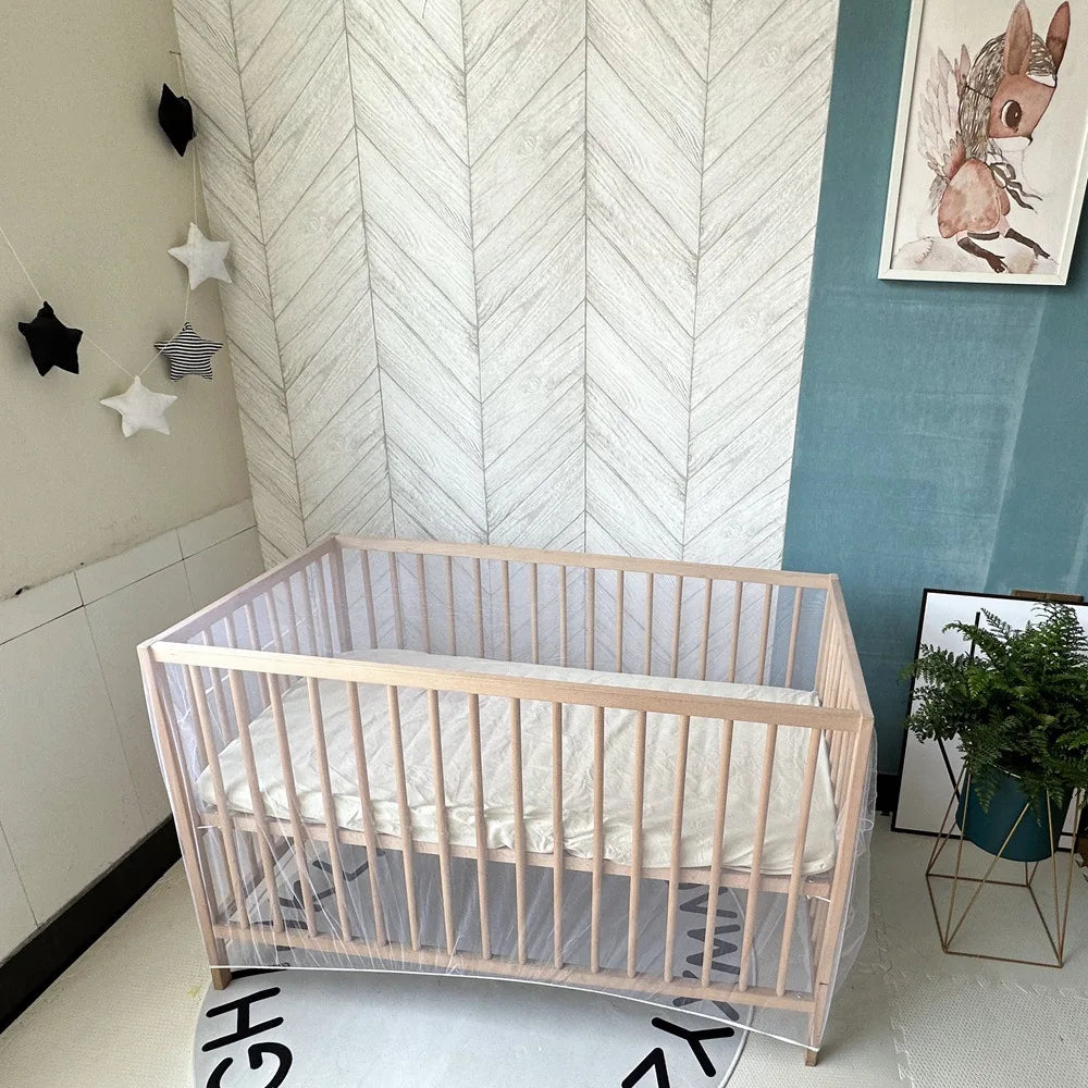 A light wood portable mosquito net crib with white bedding is displayed against a pale gray textured wall.