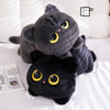 A cute black cat plush toy with yellow eyes is resting on a white surface.