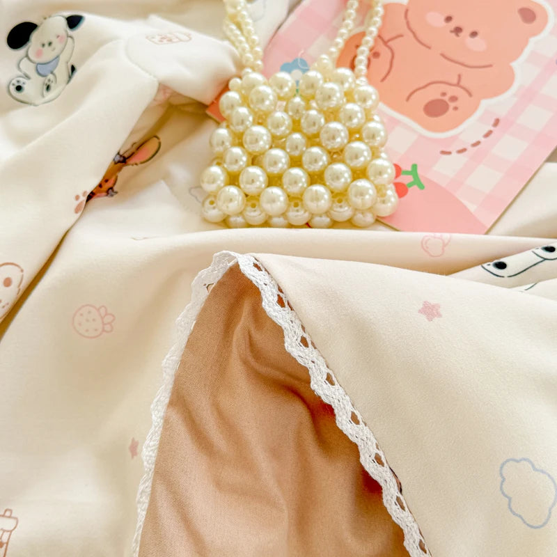 A light beige quilted blanket with pink and white patterns, featuring a pearl necklace.