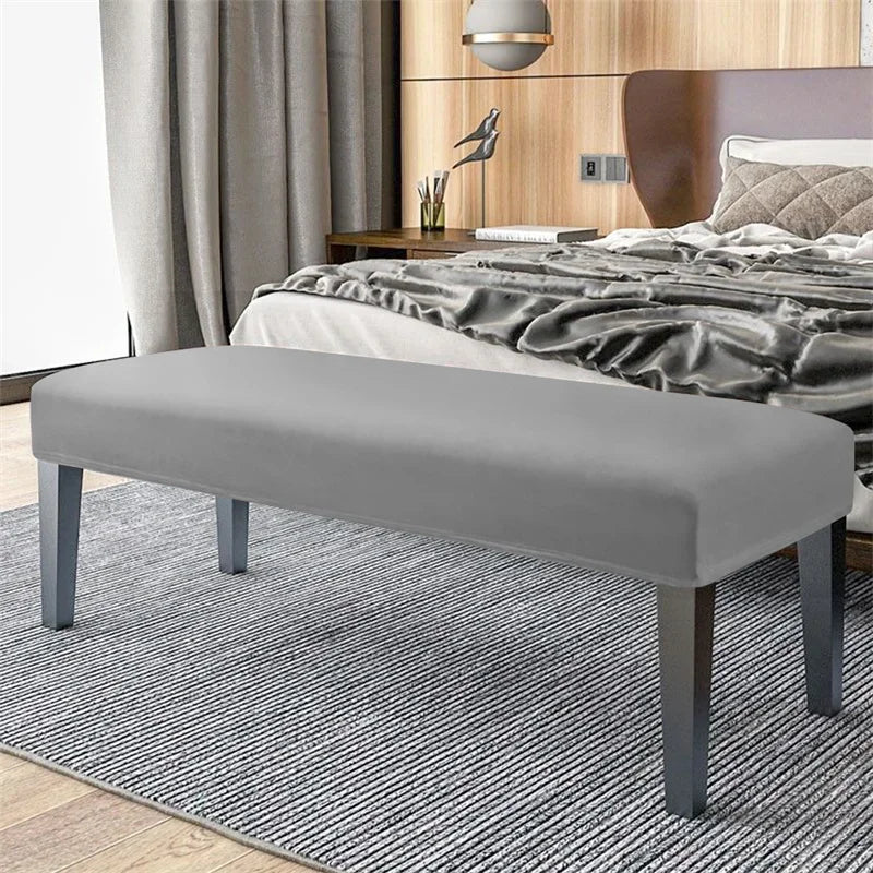 A modern gray velvet bench slipcover with secure straps placed on a light gray striped rug.