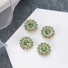 Four clusters of green and clear rhinestones on a white surface with a gray fabric in the background.