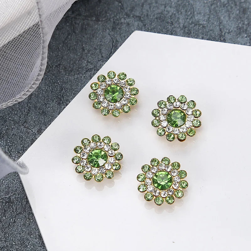 Four clusters of green and clear rhinestones on a white surface with a gray fabric in the background.