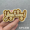 A hand holds a yellow and brown embroidered iron-on patch with the text Yeehaaw!