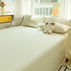 A bed with white and green striped bedding, a stuffed bear pillow, and a yellow accent on the window sill.