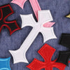 A collection of multi-color cross embroidery patches in pink, red, and black on a dark blue fabric.