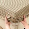 Hands are folding a beige plaid fitted sheet with a grid pattern.