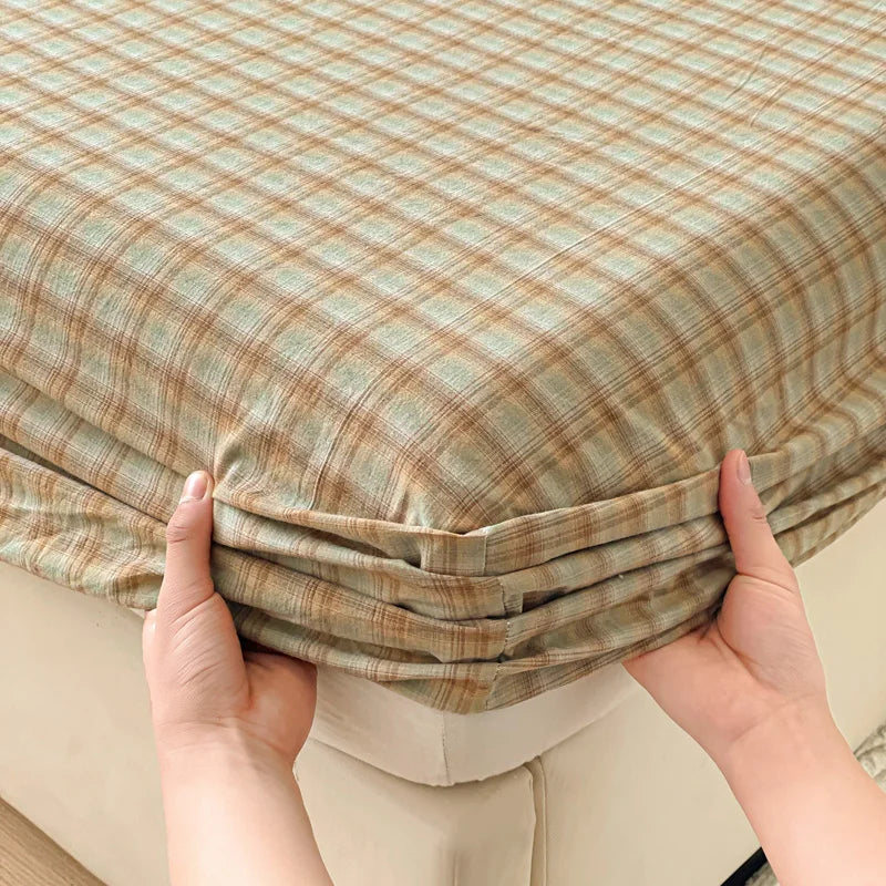 Hands are folding a beige plaid fitted sheet with a grid pattern.