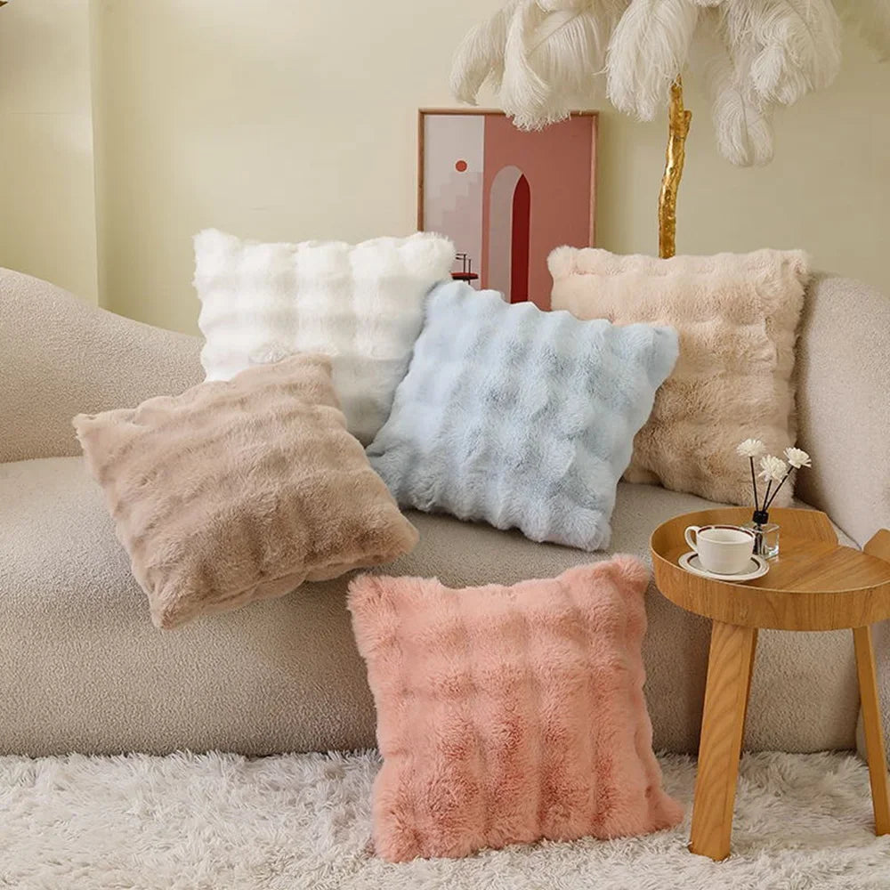 A collection of fluffy, textured cushion covers in cream, beige, pink, and light blue resting on a sofa.