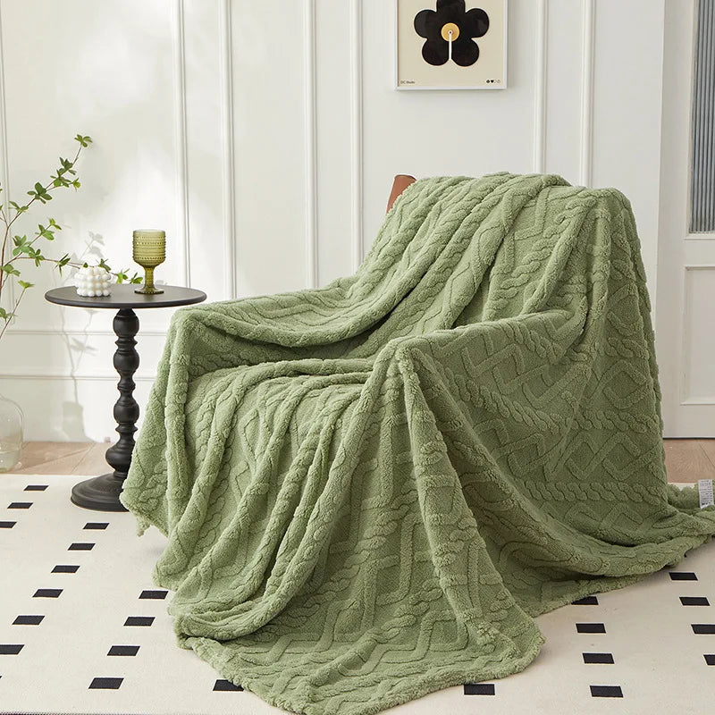 A soft, moss green plush throw blanket with a diamond jacquard pattern draped on a light rug.