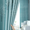 Light blue curtains featuring a white tree pattern, drawn open in a bright room.
