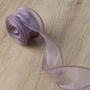 A roll of lavender organza ribbon unwinding on a wooden surface.
