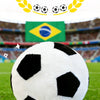 A white and black realistic football plush toy is centered on green grass with a Brazilian flag in the background.