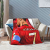 A red football jersey themed wool throw blanket draped over a light gray sofa.