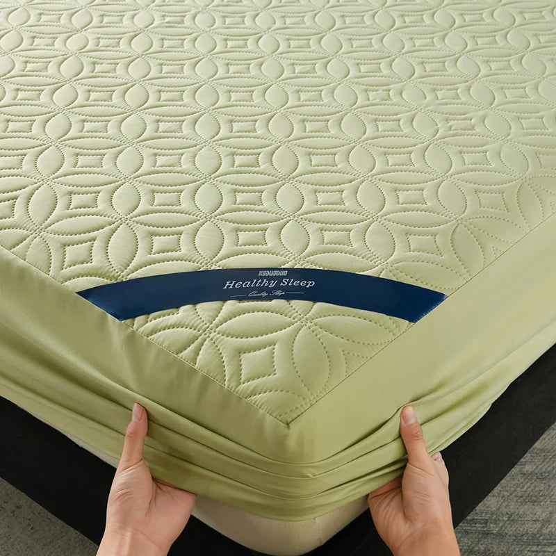 A hand is holding a light green quilted mattress protector with a blue label, showing the texture and fit.