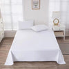 A white premium flat bed sheet is neatly laid on a bed with white pillows, set against a window with sheer white blinds.