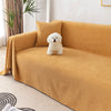 A fluffy white dog sits on a mustard yellow waterproof sofa cover blanket in a bright room.