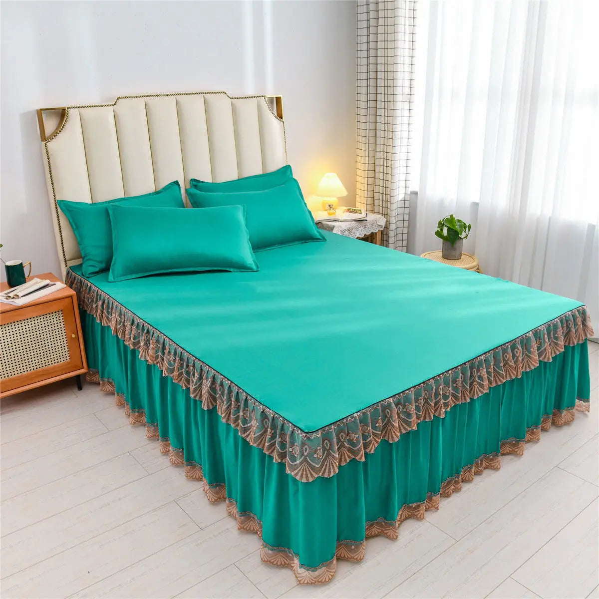 A teal luxury floral bed skirt protecting a mattress on a bed with a cream upholstered headboard.