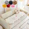 A cream-colored sofa is adorned with a white, textured mat and decorative floral accents.