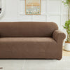 A brown sofa slipcover featuring a jacquard leaves pattern, placed in a bright room.