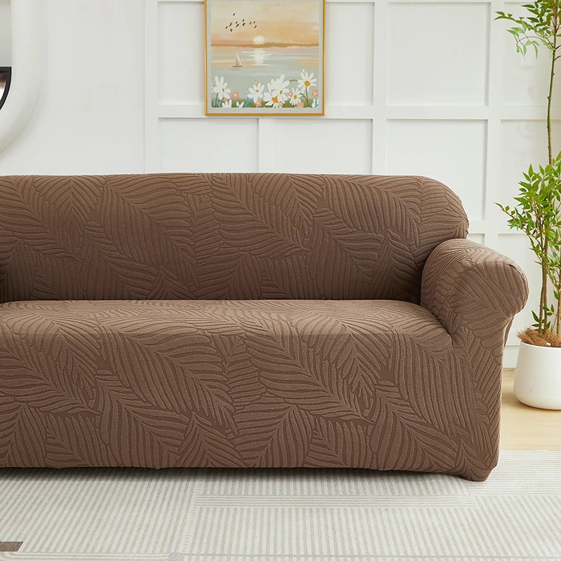 A brown sofa slipcover featuring a jacquard leaves pattern, placed in a bright room.