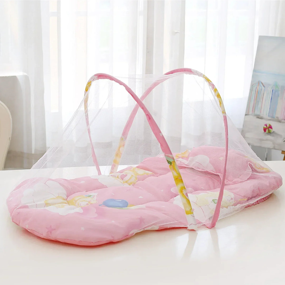 A pink portable baby crib net with soft padding and a clear mesh cover is displayed on a white surface.