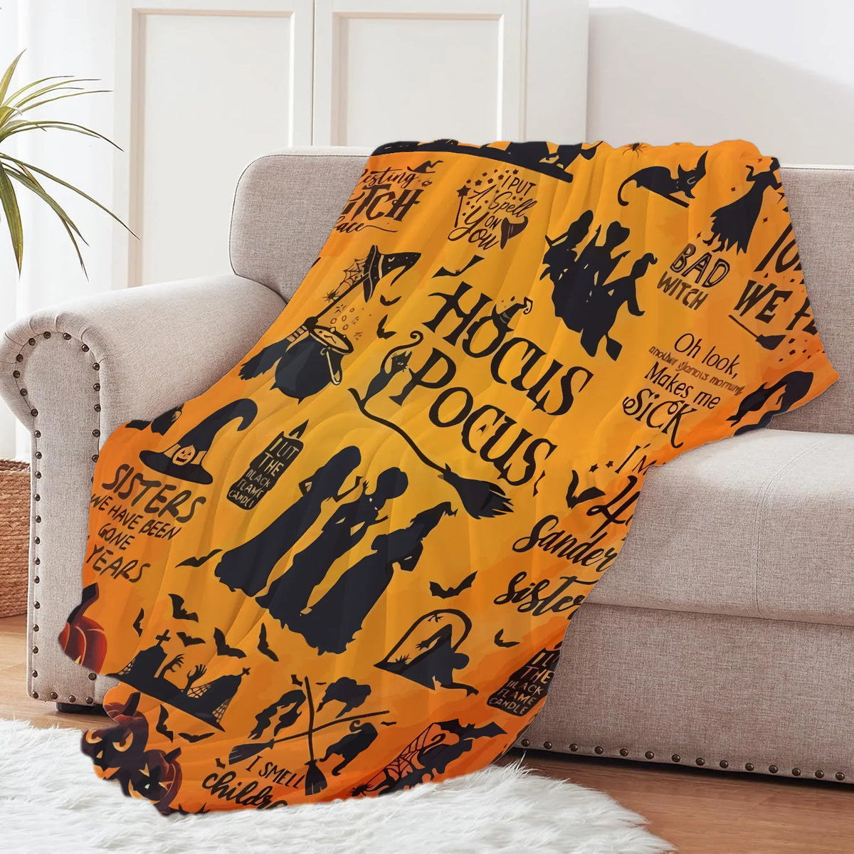 An orange flannel throw blanket featuring black witch and Halloween themed graphics draped over a light gray sofa.