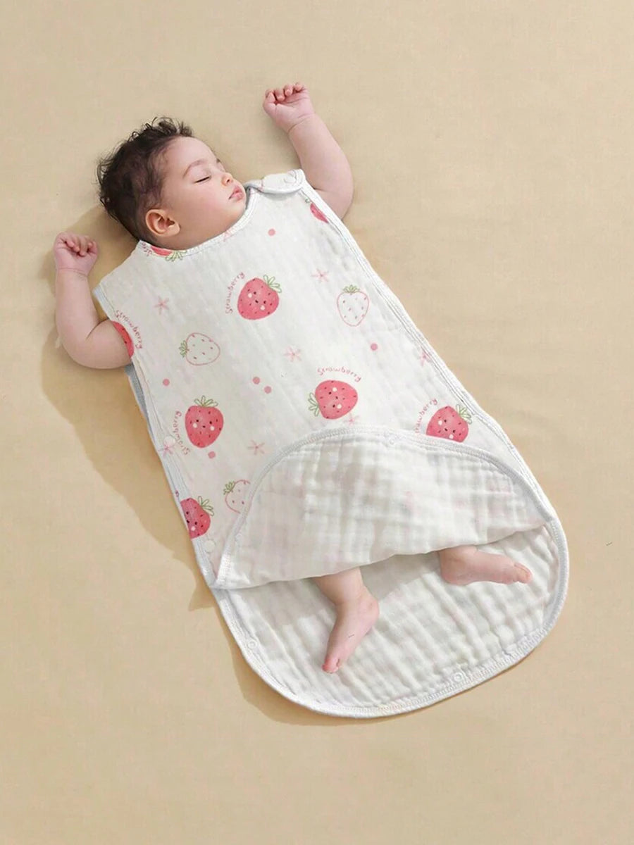 A baby is lying on a white, strawberry-patterned sleeping bag.