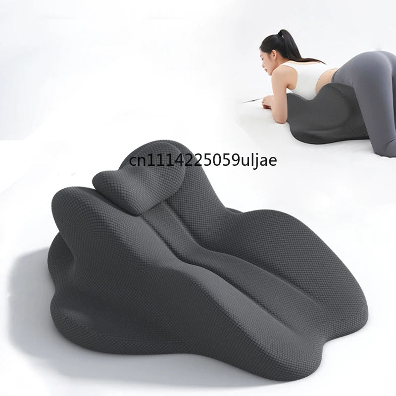 A dark gray ergonomic memory foam reading pillow is shown supporting a person's back and head for reading.