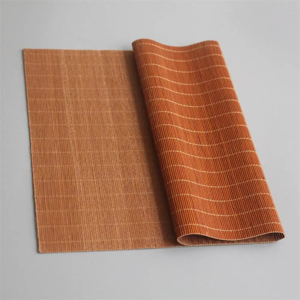 A rolled hand-woven bamboo tea mat in a warm orange color with vertical stripes.