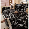 Black floral patterned sofa towel featuring white embroidery and a gold teacup on a bed.