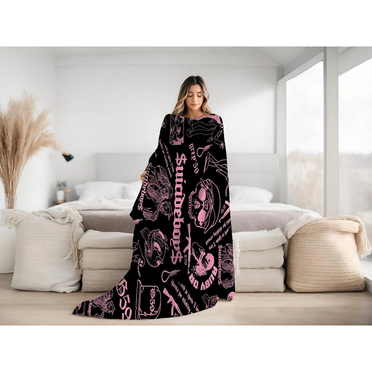 A woman models a black blanket with a retro punk print featuring skulls and text in a bright pink color.