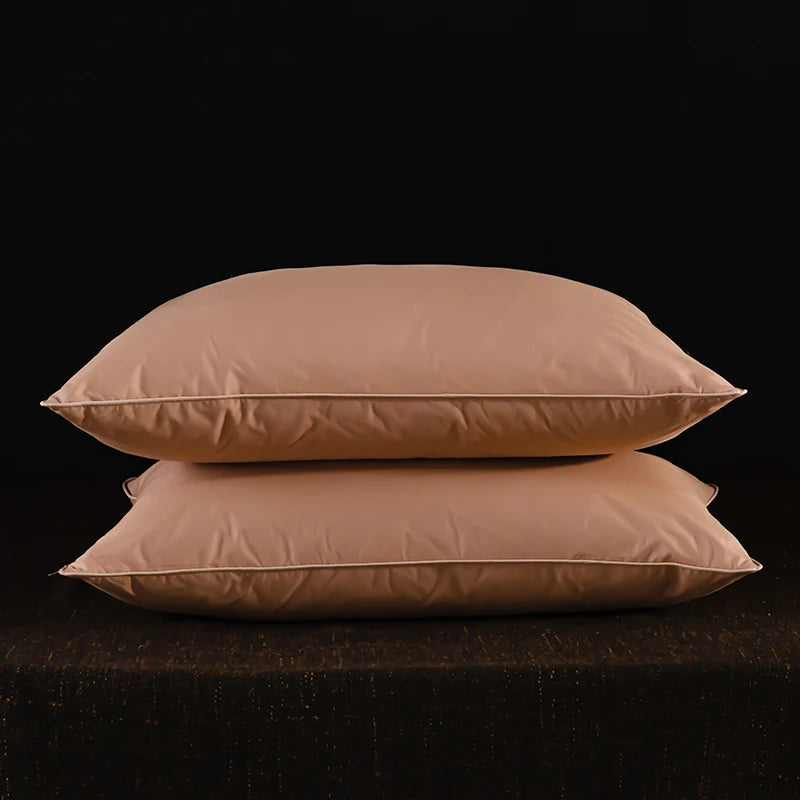 Two light beige natural goose down and feather sleeping pillows resting on a dark surface.