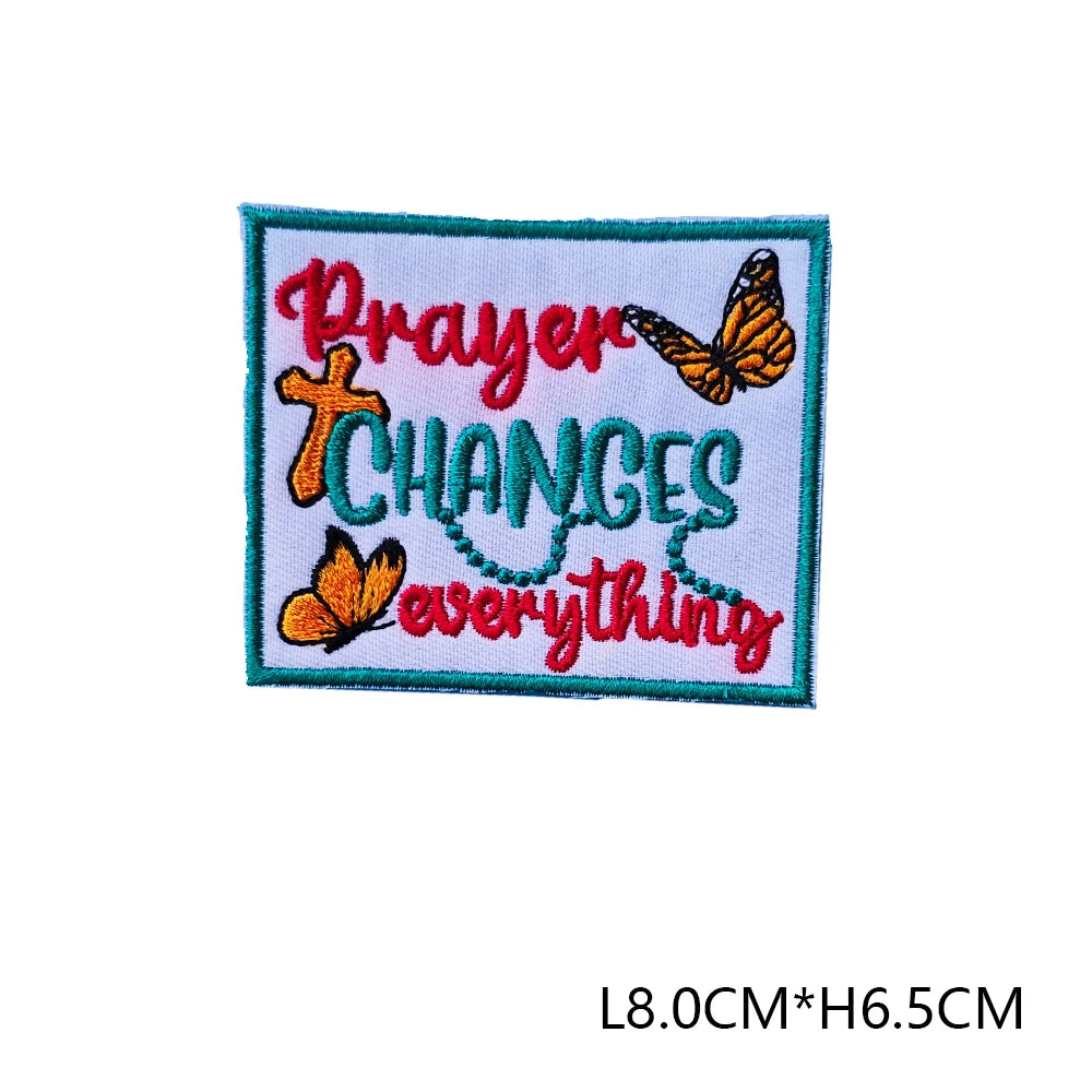 An embroidered letter patch with the text Prayer Changes everything in red and orange thread on a green fabric.