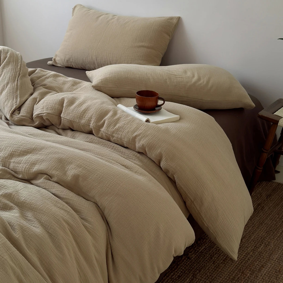 A beige duvet cover set with matching pillows and a small brown cup on a bed.
