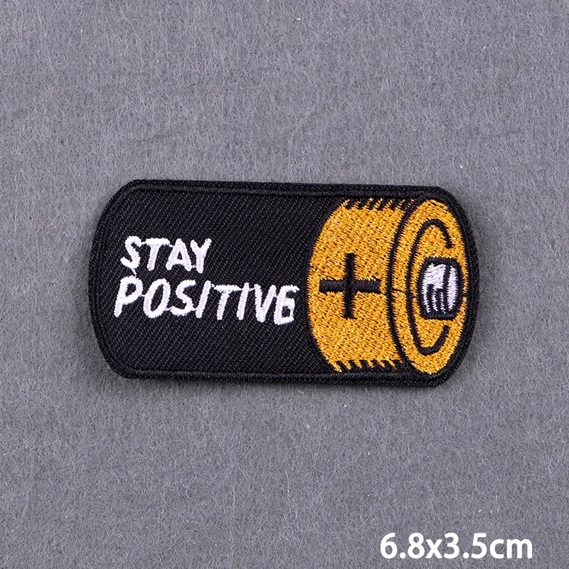 Black iron-on embroidery patch with the text STAY POSITIVE and a gold-colored spool design