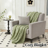 A light gray armchair draped with a green plush blanket on a white rug.