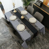 A rectangular gray tablecloth set for dining featuring black and gold patterned runners and white plates.