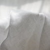 A close-up of a white pure linen flat sheet fabric draped softly, showing its texture and weave.