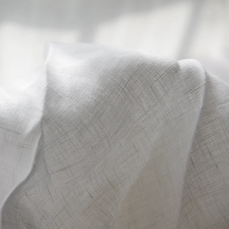 A close-up of a white pure linen flat sheet fabric draped softly, showing its texture and weave.