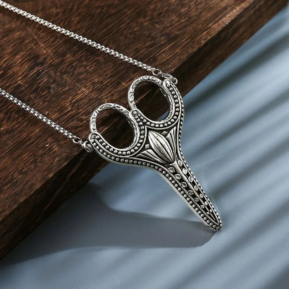 Vintage stainless steel sewing scissors with an ornate handle resting on a dark wooden surface.
